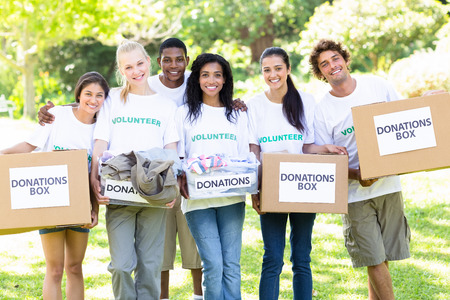 Group portrait of happy volunteers carrying donation boxes in park
