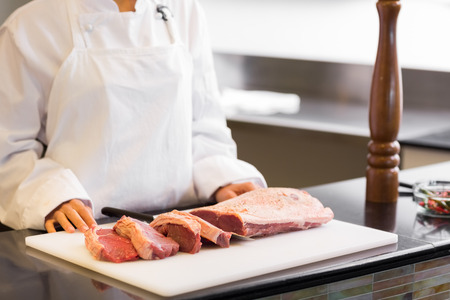 Closeup mid section of a chef with cut meat pieces in the kitchenの写真素材