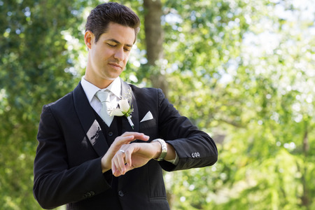 Young smart groom checking time in gardenの写真素材