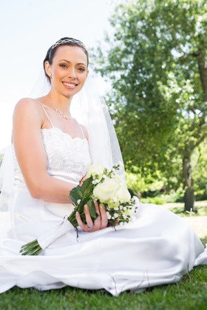 Portrait of confident bride holding flower bouquet while sitting in gardenの写真素材
