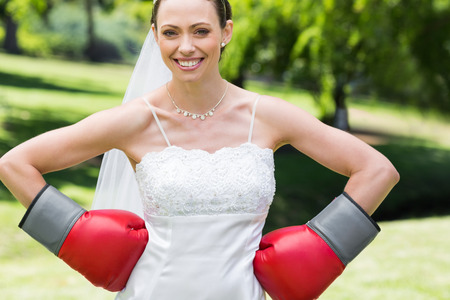Portrait of young bride wearing boxing gloves with hands on waist in gardenの写真素材