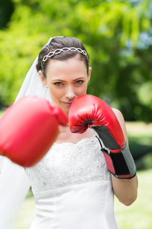 Portrait of confident young bride with boxing gloves punching in gardenの写真素材