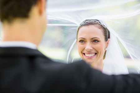Young groom lifting bridal veil in gardenの写真素材