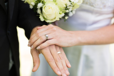 Closeup of bride and groom showing wedding rings touching handsの写真素材