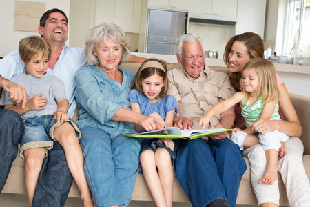Happy multigeneration family reading storybook in living room at homeの写真素材