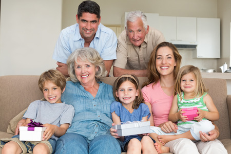Portrait of happy siblings holding gifts with family in living room