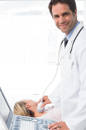 Portrait of confident male doctor using sonogram on neck of female patientの写真素材