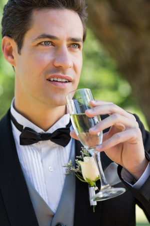 Closeup of thoughtful groom drinking champagne in gardenの写真素材