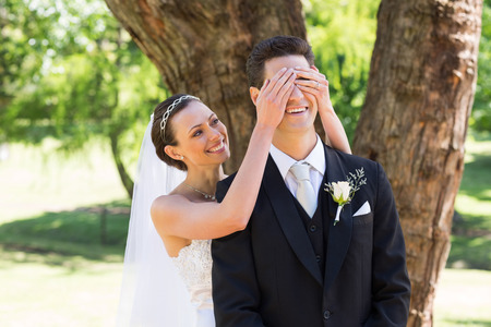 Happy young bride covering eyes of groom in gardenの写真素材