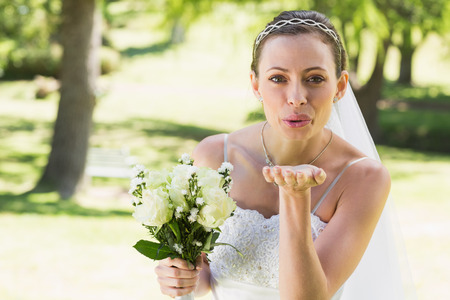 Portrait of beautiful bride with bouquet blowing kiss in gardenの写真素材