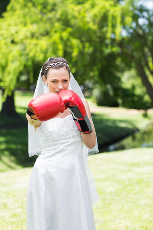 Portrait of beautiful young bride with boxing gloves punching in parkの写真素材