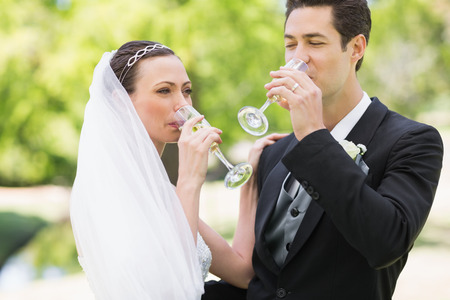 Newlywed couple drinking champagne in the parkの写真素材