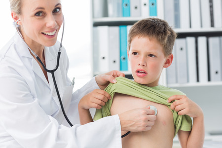 Confident female doctor examining boy with stethoscope in clinicの写真素材