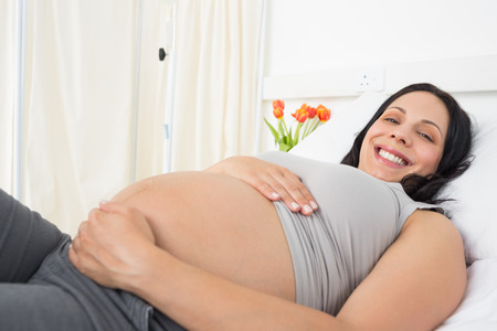 Portrait of happy pregnant woman lying in bed at hospital