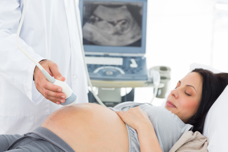 Midsection of male doctor performing ultrasound test on pregnant woman in hospitalの写真素材