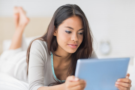 Pretty girl lying on bed using her tablet pc in her bedroom at homeの写真素材