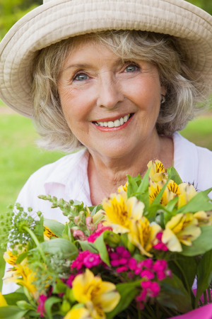 Close-up portrait of a smiling mature woman holding flowers at the parkの写真素材