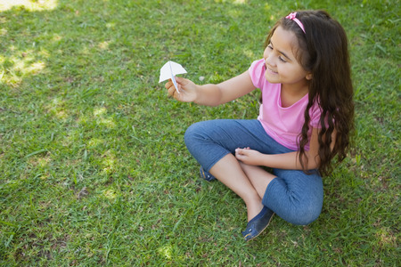 High angle view of a happy girl playing with a paper plane at the parkの写真素材