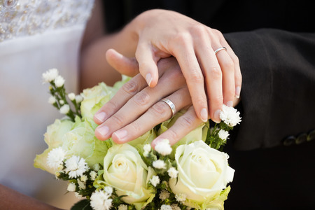 Close-up mid section of a newlywed couple with wedding rings and bouquetの写真素材