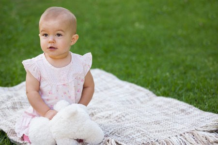 Cute little baby with stuffed toy sitting on blanket at the parkの写真素材
