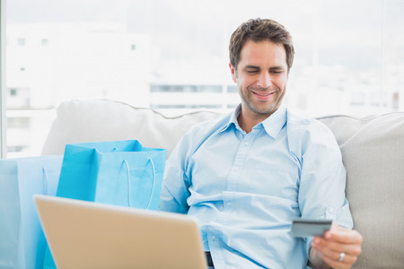 Handsome man using laptop sitting on sofa shopping online at home in the living roomの写真素材