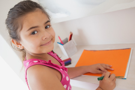 Side view portrait of a young girl drawing on orange paper at homeの写真素材
