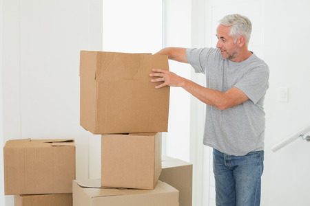 Smiling man looking at cardboard moving boxes in new homeの写真素材