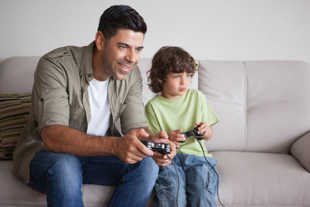 Cheerful father and son playing video games in the living room at home