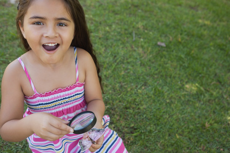 Portrait of a young girl examining a butterfly with magnifying glass at the parkの写真素材