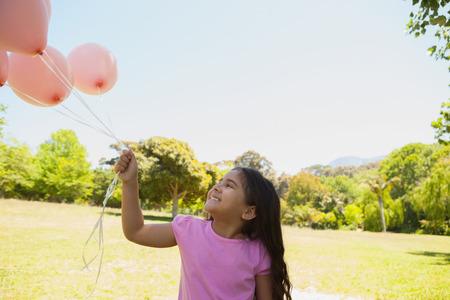 Cute little girl playing with pink balloons at the parkの写真素材