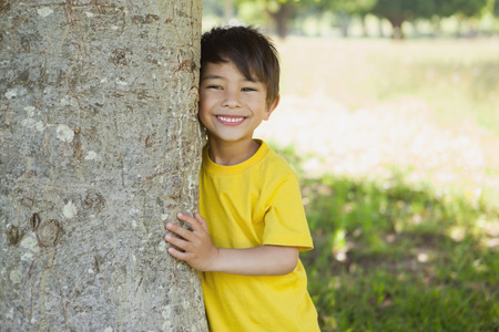 Portrait of a cheerful young boy standing by tree at the parkの写真素材