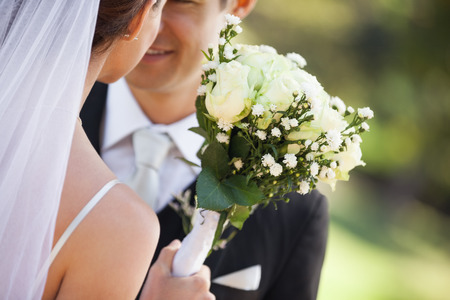 Close-up mid section of a young newlywed couple with bouquet in the parkの写真素材