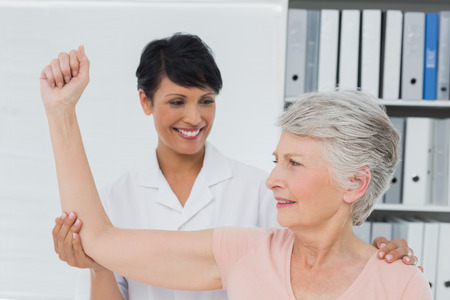 Female physiotherapist assisting senior woman to stretch her hand in the medical officeの写真素材