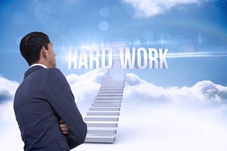 The word hard work and unsmiling asian businessman with arms crossed against shut door at top of stairs in the skyの写真素材