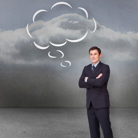 Young businessman standing cross-armed with speech bubble against clouds in a roomの写真素材