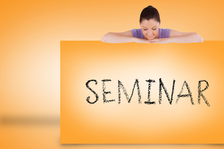 Pretty brunette showing card with seminar against orange backgroundの写真素材