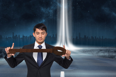 Unsmiling businessman carrying large key against road leading out to the horizon with light beamの写真素材