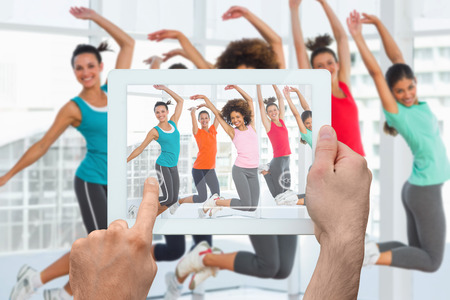 Hand holding tablet pc against zumba class in gymの写真素材