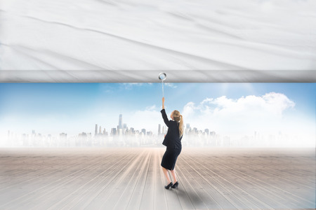Businesswoman pulling a white screen against cityscape on the horizonの写真素材