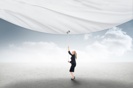 Businesswoman pulling a white screen against cloudy sky backgroundの写真素材