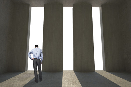 Businessman with hand on hip against light shining into dark roomの写真素材