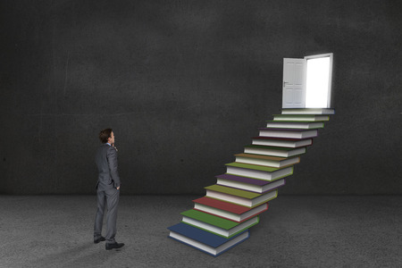 Thinking businessman against steps made from books leading to door in grey roomの写真素材