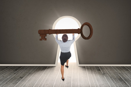 Businesswoman carrying large key against door revealing bright lightの写真素材