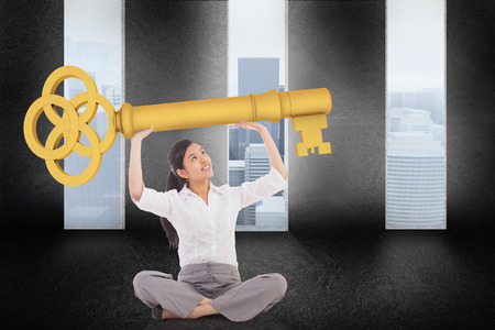 Businesswoman sitting cross legged carrying large key against graphic with doors and a light bulb on gloomy countrysideの写真素材
