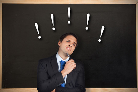 Thinking businessman holding pen against chalkboard with wooden frameの写真素材