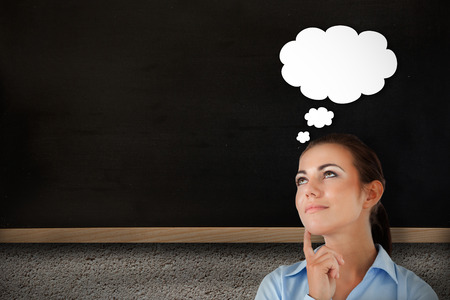 Thinking businesswoman looking upwards against chalkboard on grey wallの写真素材