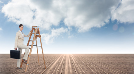 Businesswoman climbing career ladder with briefcase and looking at camera against cloudy sky backgroundの写真素材