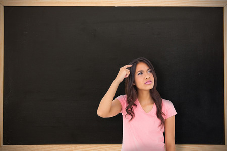 Pretty brunette thinking against chalkboard with wooden frameの写真素材