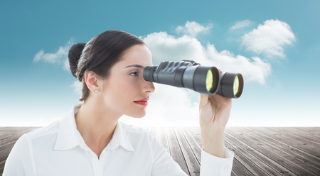 Business woman looking through binoculars against cloudy sky backgroundの写真素材