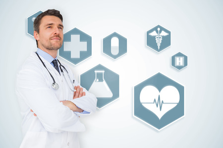 Handsome young doctor with arms crossed against blue medical interface with iconsの写真素材